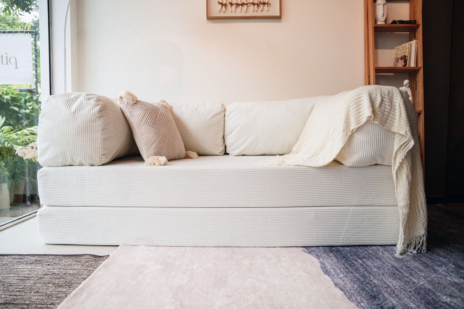 A cream corduroy Cloud Sofa against a warm wall, a woven throw folded over one end.